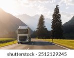 Scenic front view modern white semi-trailer truck driving stunning alpine mountain road warm sunset light sky background. Freight cargo logistics transportation vehicle freeway route evening sunlight