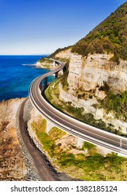 Scenic Grand Pacific drive highway passing Sea Cliff Bridge around steep sandstone cliff on Pacific coast of Australia - aerial vertical view over the road.