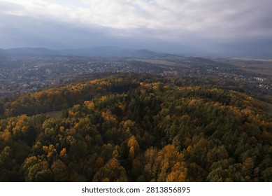 Scenic high angle view of rolling hills covered with dense colorful autumn forests, with a small town in a misty valley under dramatic sky in Walbrzych, Poland.