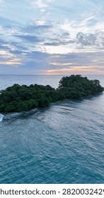 Scenic high-angle view capturing a small, lush green islet surrounded by turquoise sea water off the coast of Koh Chang, Thailand, with a soft sunset glowing on the horizon.
