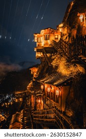Camino panorámico iluminado que serpentea por la ciudad del valle de Wangxian por la noche, combinando formaciones rocosas naturales y arquitectura tradicional china en un entorno de montaña tranquilo.