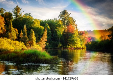 A scenic lake or river during a light rain displaying a rainbow in the mist on an autumn day close to sunrise or sunset. - Powered by Shutterstock