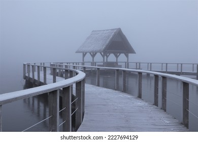 Scenic lake side view with wooden jetty in dense fog in winter. - Shutterstock ID 2227694129