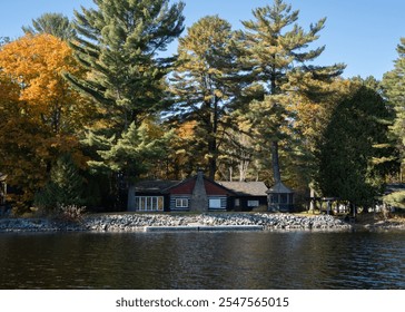 Scenic lakeside cabin surrounded by vibrant autumn foliage and tall pine trees, reflecting tranquility and nature's beauty. - Powered by Shutterstock