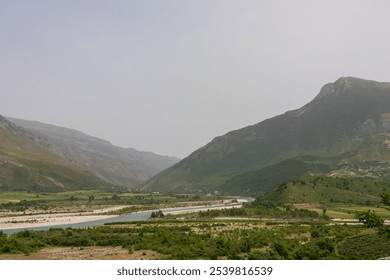 Scenic landscape in Albania, featuring Vjosa River winding through valley surrounded by mountains. Stream is wide and meandering with sandy bed and clear water. Lush green vegetation lines the banks - Powered by Shutterstock