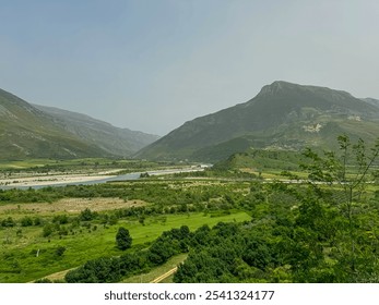 Scenic landscape in Albania, featuring Vjosa River winding through valley surrounded by mountains. Stream is wide and meandering with sandy bed and clear water. Lush green vegetation lines the banks - Powered by Shutterstock