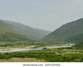 Scenic landscape in Albania, featuring Vjosa River winding through valley surrounded by mountains. Stream is wide and meandering with sandy bed and clear water. Lush green vegetation lines the banks - Powered by Shutterstock