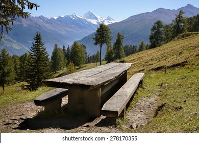 Scenic landscape with empty rustic picnic table and benches made of lumber on a grassy slope with coniferous trees and snow-capped Matterhorn mountain at the horizon, in Valais, Alps, Switzerland.