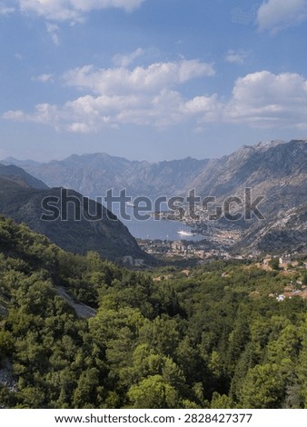 Scenic landscape featuring cliffs, forests, a coastal town, and a calm sea in a protected bay, distant mountains and a clear azure sky over blue water