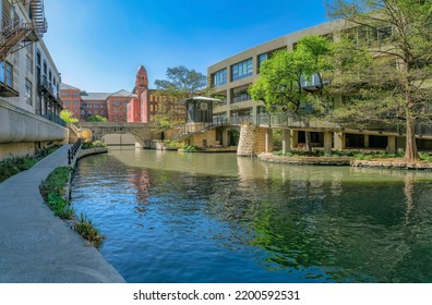 Scenic Landscape Of The River Walk In San Antonio Texas On A Sunny Day. The Paved Trails, Bridge And Buildings Have A Relaxing View Of The Calm Canal And Blue Sky.