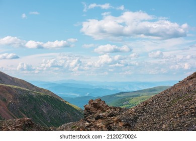 Scenic landscape with sunlit stone outliers with view to mountain vastness under cloudy sky. Colorful mountain scenery with sharp rocks on mountain pass under clouds in blue sky at changeable weather.