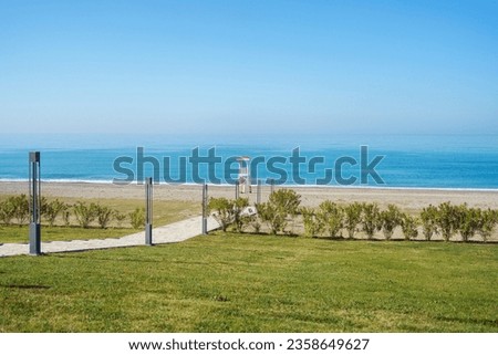 Scenic landscape view of concrete pathway to the empty bay watch tower on a lonely seaside beach. Scenery landscape of a sea ocean shore with wooden abandoned lifeguard tower