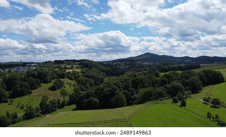 Scenic landscape view of Ölberg in Siebengebirge, Germany. Rolling hills, lush forests, and green meadows under a dramatic cloudy sky, captured from Stieldorf. - Powered by Shutterstock