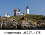 Scenic lighthouse on rocky cliff with clear blue sky. Lighthouse stands tall on cliff, surrounded by small buildings. Picturesque lighthouse and cliff view. Coastal landscape view.