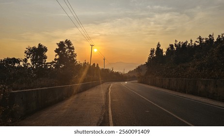 "Scenic morning sunrise view from a rural road, surrounded by lush green fields and distant hills. Golden sunlight pierces through misty skies, creating a peaceful and picturesque countryside ambiance - Powered by Shutterstock