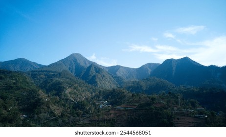 A scenic mountain landscape with lush green terraced fields, scattered villages, and forested hills under a bright blue sky - Powered by Shutterstock