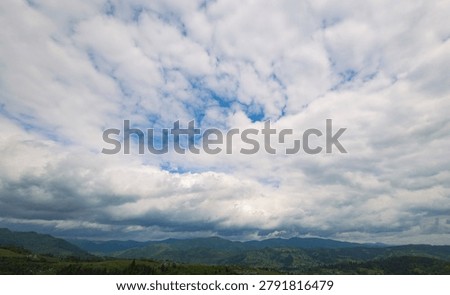 Scenic mountain landscape under a dramatic cloudy sky, beautiful summer day with white and grey cumulus clouds over green hills and pine forest tree silhouettes