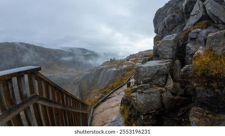 A scenic mountain landscape with a wooden staircase leading down a rocky path. Misty clouds hover over the distant hills, creating a serene and atmospheric view. - Powered by Shutterstock