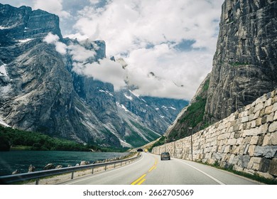 Scenic Mountain Road with Dramatic Cliffs and Lush Valley Leading to Cloudy Peaks in a Serene Landscape