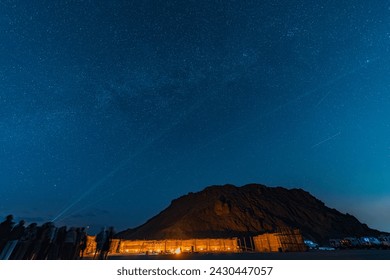 Scenic night photo of tourists star gazing at Red Sea Hills mountain, Sahara desert. Group of tourists look at starry sky. Guide highlight Milky Way stars by green laser. Long exposure night photo