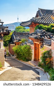 Scenic Old Narrow Street And Traditional Korean Houses Of Bukchon Hanok Village In Seoul, South Korea. Seoul Tower On Namsan Mountain Is Visible On Blue Sky Background. Beautiful Cityscape.