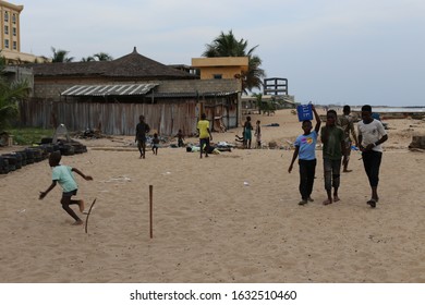 Scenic outdoor view of young children playing football on the sandy beach located in Cotonou city, Benin, West Africa. December, 1, 2019. Garbage and waste visible, not far from the people.