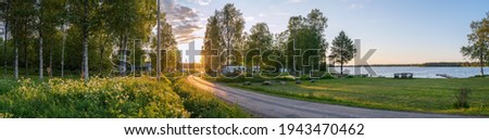Scenic panorama of Swedish birch forest, summer village, lake and beautiful Sunset lighting on countryside road. Sweden.