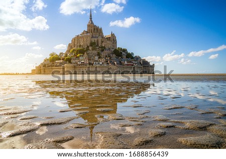 Scenic panoramic view of famous Le Mont Saint-Michel tidal island with historic abbey on top of impressiv rock on a beautiful sunny day with blue sky and clouds in summer, Normandy, northern France