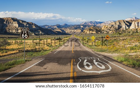 Scenic panoramic view of long straight road on famous Route 66 with historical street signs and paintings in classic american wild western mountain scenery in beautiful golden evening light at sunset