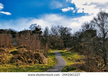 Scenic pathway through a lush park with rocky outcrops and vibrant blue sky with fluffy clouds at Brimham Rocks, in North Yorkshire