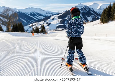 Scenic portrait view kid beginner skier close-up downhill start line rows freshly prepared groomed ski slope piste bright warm morning sunrise sky background.  mountain landscape winter resort