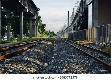 A scenic railway track surrounded by greenery and urban structures, captured from a low angle perspective. The image highlights the contrast between nature and urban development, with a clear blue sky - Powered by Shutterstock