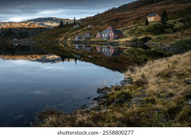 Scenic reflection of colorful hillside houses on a calm lake, surrounded by rugged mountains and autumn vegetation in a tranquil Nordic landscape. - Powered by Shutterstock