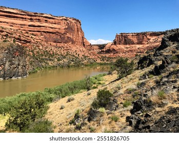 Scenic River Canyon Landscape with Rugged Red Rock Cliffs and Vegetation under a Clear Blue Sky - Powered by Shutterstock