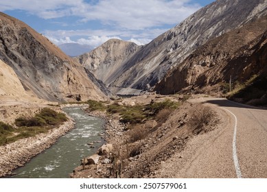 A scenic road winds through a dramatic canyon in the Peruvian Andes, following the path of a swiftly flowing river. The rugged, rocky cliffs rise steeply on either side, showcasing the breathtaking . - Powered by Shutterstock