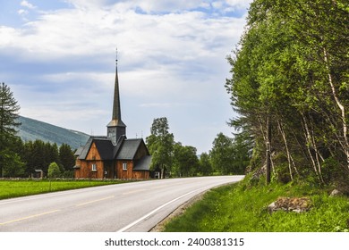 A scenic road winds towards the ancient Kvikne kirke in Innlandet, Norway, a wooden church with a tall spire, gracefully encircled by green trees, depicting a serene and historic tableau
