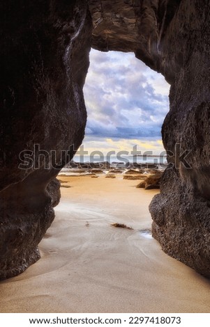 Scenic sandstone sea cave entering sandy beach in Caves beach coastal town on Pacific coast of Australia at sunrise.