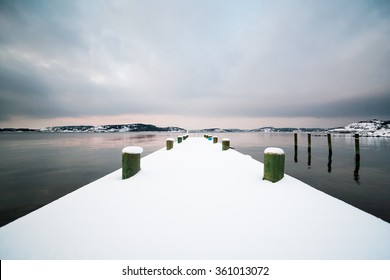 A scenic Scandinavian (Swedish) winter landscape with a pier in southern Gothenburg, Sweden covered in snow in December.
