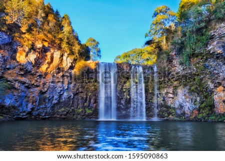 Scenic section of lower Dangar falls falling down to fresh water pool cutting through vulcanic rocks in Dorrigo national park under clear blue sky in soft morning light.
