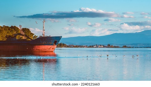 A scenic shot of a lake with an abandoned ship on it, while birds fly over the lake water on a sunny day - Shutterstock ID 2240121663
