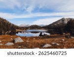 A scenic shot of a  lake surrounded by green trees and a mountain range on a sunny day