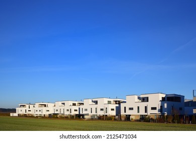 Geräumige Aufnahme von neuen Einfamilienhäusern, die eine kleine Siedlung am Rande eines grünen Raumes bilden, vor dem Hintergrund eines blauen Himmels mit Platz für Text.