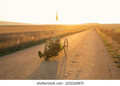 Scenic Shot of a Young Man Athlete with disability Riding a Handcycle. Adaptive Exercise Outdoors at Sunset . High quality photography. - Powered by Shutterstock