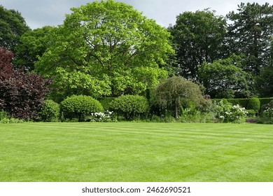 Scenic summertime view of an attractive English style landscape garden with a fresh mowed grass lawn, green leafy trees and colourful flowers in bloom - garden and nature themed photograph in colour - Powered by Shutterstock