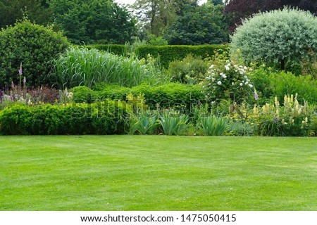 Scenic Summertime View of a Beautiful English Style Landscape Garden with a Green Mowed Lawn, Leafy Trees and Colourful Flower Bed