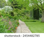 A scenic summertime view of a stone paved path through an attractive English style garden with a flowers in bloom and green leafy plants