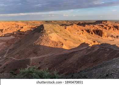 Scenic sunrise view of the Mongolian landscape across the glowing red mountains of the famous Mongolian Flaming Cliffs and a distant remote ger camp in the Gobi Desert to the horizon