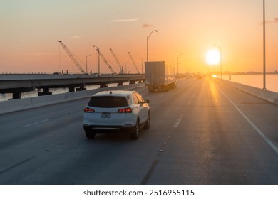 Scenic sunset drive on a coastal highway with vehicles traveling towards a radiant horizon, showcasing beautiful evening light and long shadows. - Powered by Shutterstock