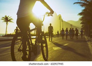 Scenic Sunset View Of Cyclist Riding His Bike Along The Ipanema Beach Promenade In Rio De Janeiro, Brazil 