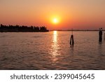 Scenic sunset view on San Michele island at Venetian lagoon in Venice, Veneto, Northern Italy, Europe. Reflection in the water creating romantic atmosphere. Orange red sky. Silhouette of landmarks